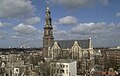 Seitliche Farbfotografie in der Obersicht einer braunen Kirche mit weißen Ornamenten um das Kirchenschiff und den Dachgiebeln. Der Turm mit goldener Haube und Dachlaterne steht links.