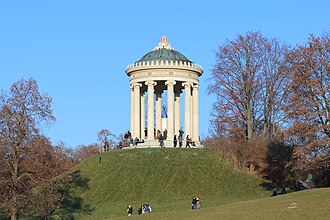 Monopteros auf künstlichem Hügel im Englischen Garten in München. 1832 wurde auf dem ursprünglich flachen Gelände ein 15 Meter hohes Fundament aus Backstein geschaffen, im Laufe mehrerer Jahre durch Erdaufschüttung überhügelt und darauf der Rundtempel errichtet.