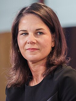 Farbfotografie im Porträt von Annalena Baerbock, die links an der Kamera vorbei schaut und lächelt. Sie trägt ein schwarzes Oberteil. In der Bildunterschrift ist noch eine Handsignatur von Baerbock.